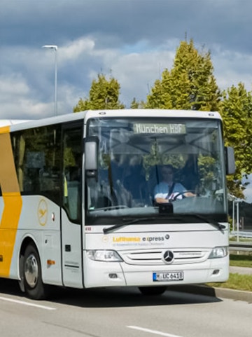 Lufthansa Express bus traveling to Munich HBF on a tree-lined road.