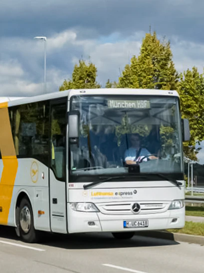 Lufthansa Express bus traveling to Munich HBF on a tree-lined road.