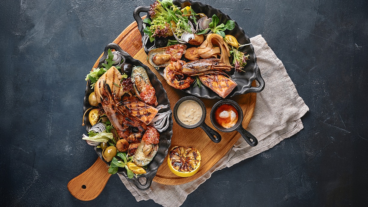 Grilled seafood platter with shrimp, salmon, mussels, and salad on a wooden board.