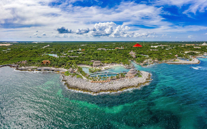 Aerial view of Xcaret Park's coastline with lush greenery and turquoise waters in Mexico.