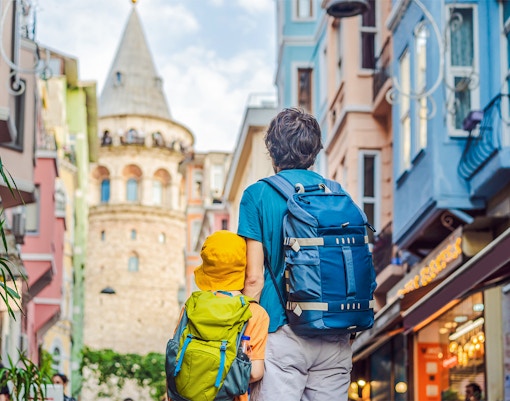 Father and son with backpacks facing Galata Tower in Istanbul.