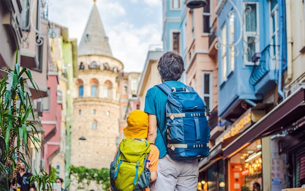 Father and son with backpacks facing Galata Tower in Istanbul.