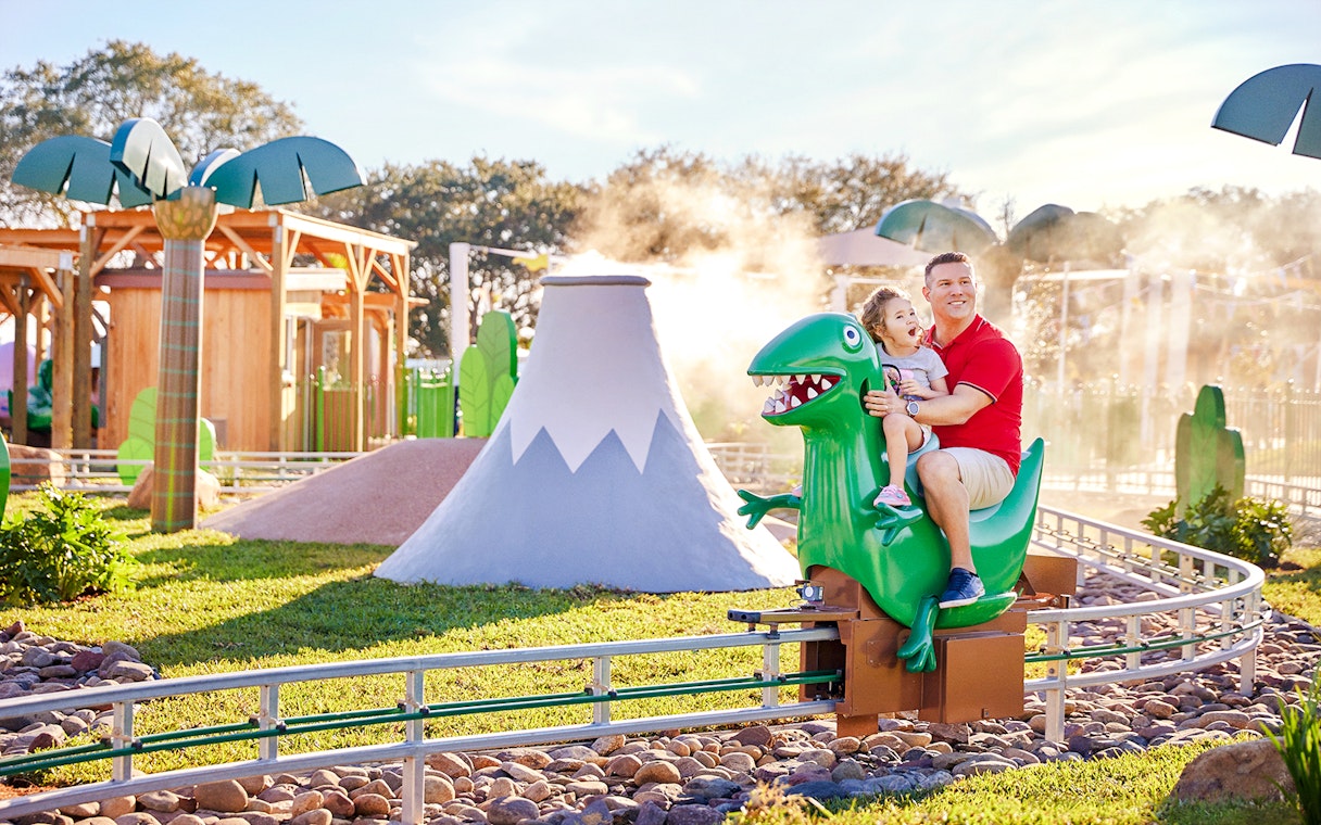 Father and child riding a dinosaur attraction at Peppa Pig Park, Guntzburg.