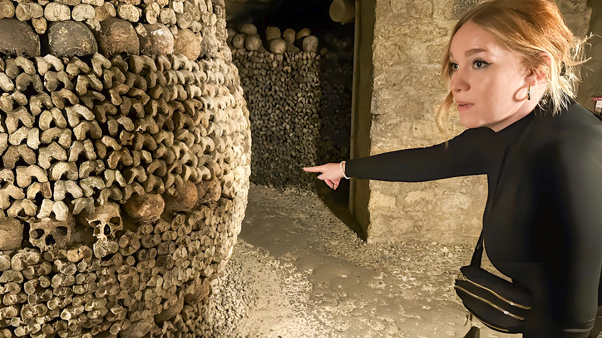 Guide pointing at skulls and bones in Paris Catacombs during small group tour.