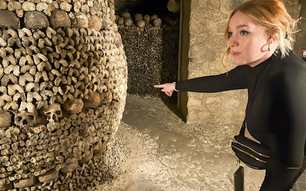 Guide pointing at skulls and bones in Paris Catacombs during small group tour.