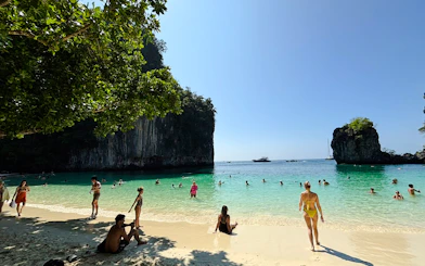 Tourists enjoying the beach and clear waters at Hong Islands, Krabi, with longtail boats in the distance.