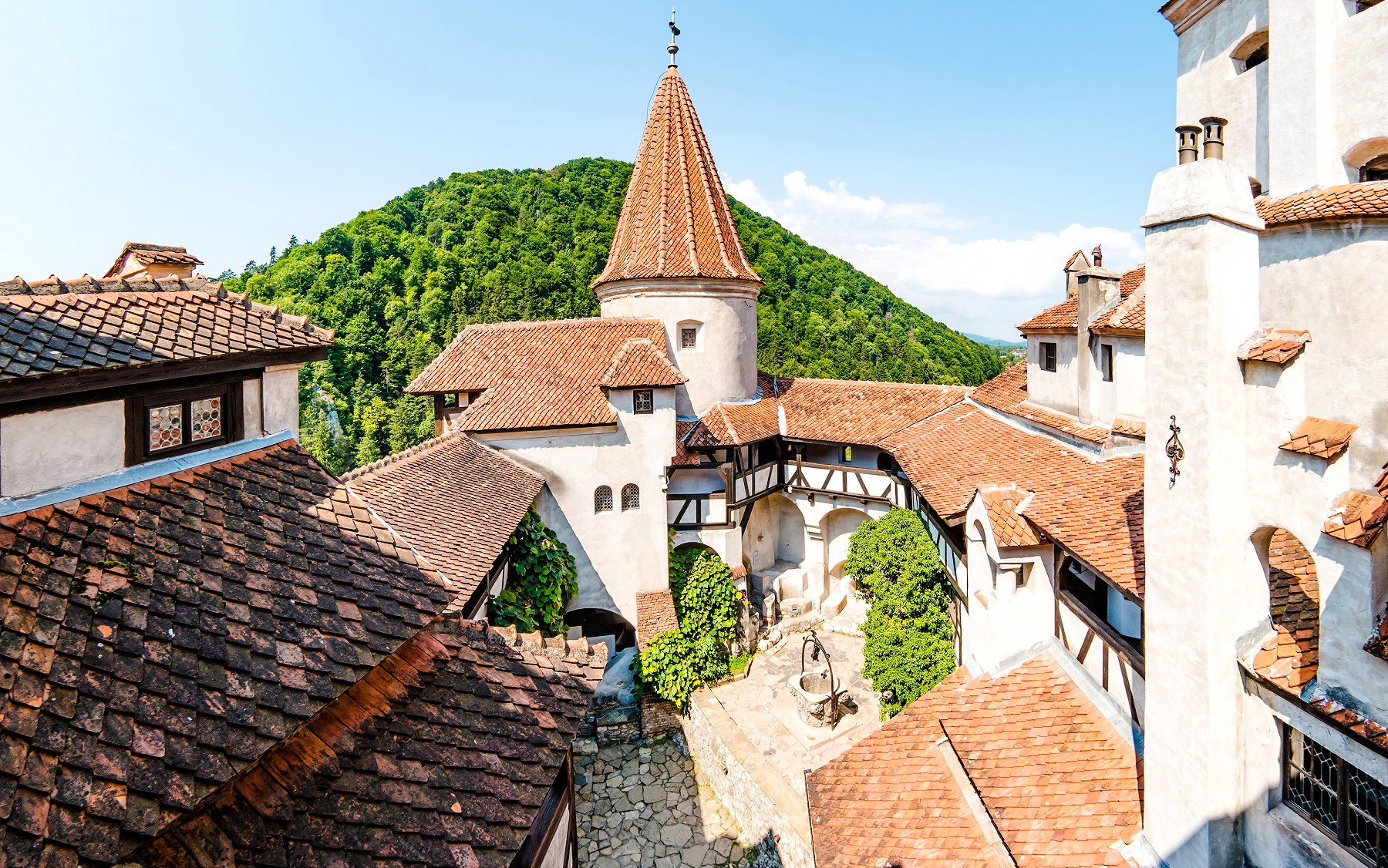 Bran Castle courtyard with red-tiled roofs and central well, surrounded by lush hills in Romania.