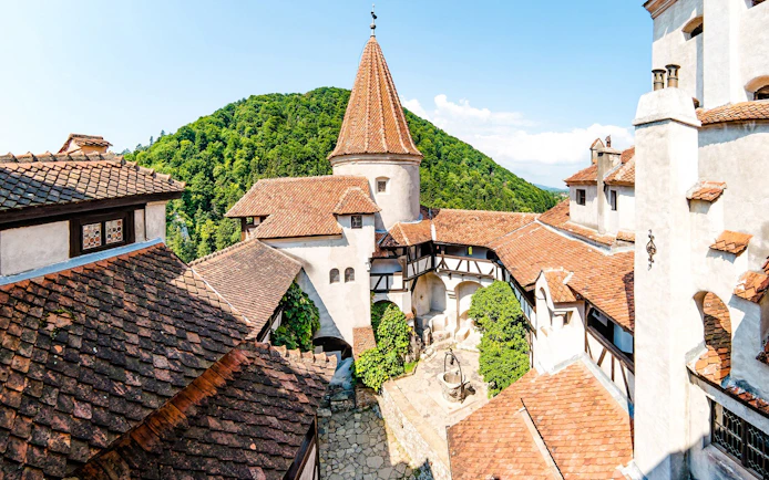 Bran Castle courtyard with red-tiled roofs and central well, surrounded by lush hills in Romania.