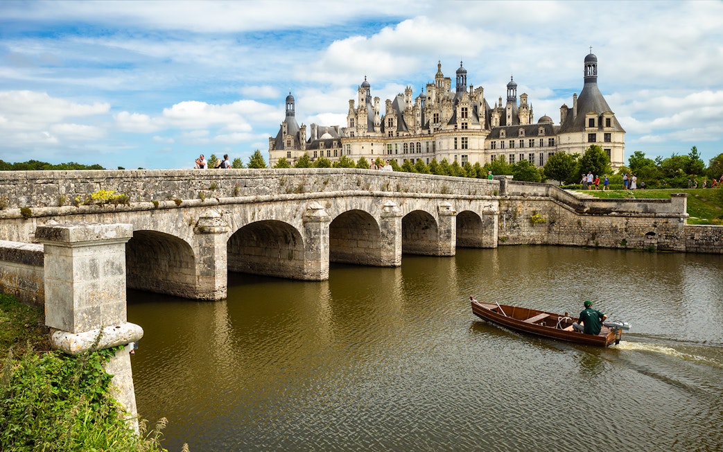 Loire Valley Château with stone bridge and boat on river.