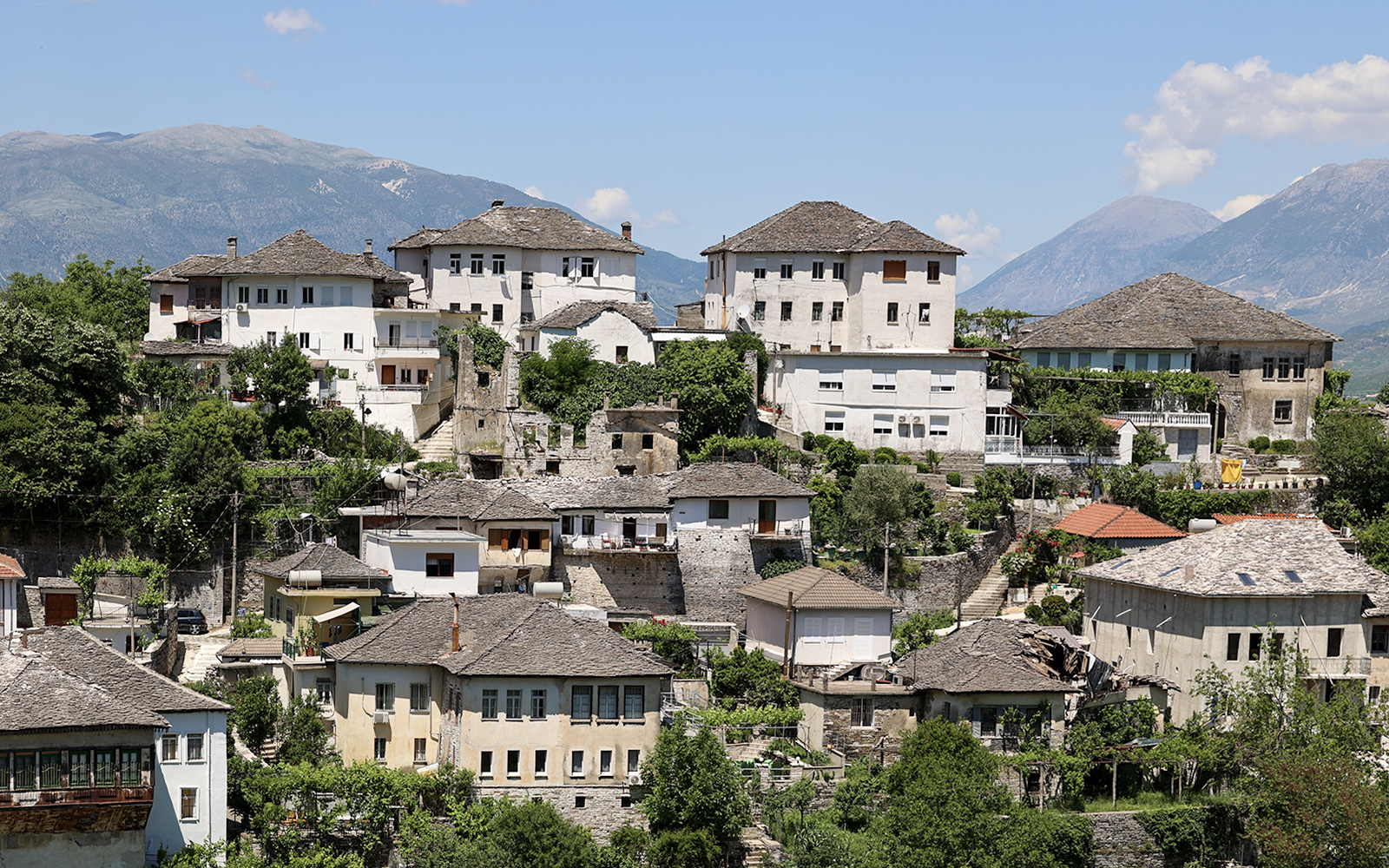 Historic stone houses in the old town of Gjirokastra, Albania, with mountain backdrop.