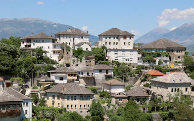 Historic stone houses in the old town of Gjirokastra, Albania, with mountain backdrop.