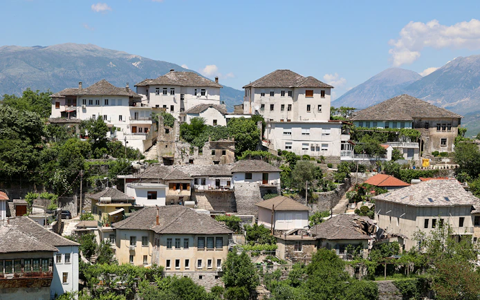 Historic stone houses in the old town of Gjirokastra, Albania, with mountain backdrop.