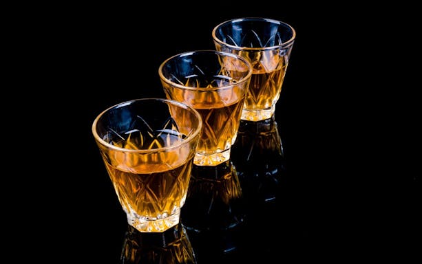 Three glasses of amber liqueur on a black surface, Vodka and Liqueurs Tour in Krakow.