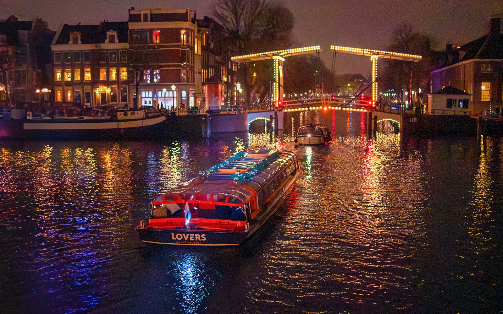 Canal cruise boat under illuminated bridge during Amsterdam Light Festival.