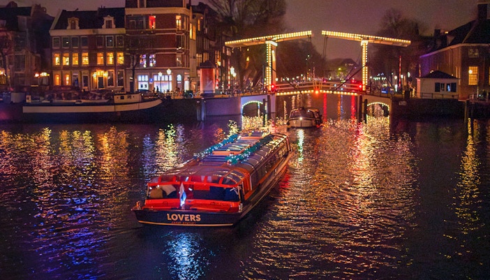 Canal cruise boat under illuminated bridge during Amsterdam Light Festival.