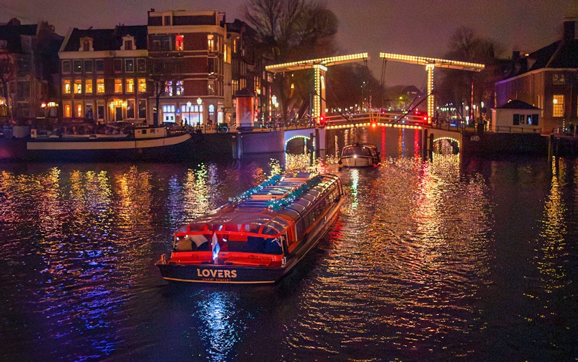 Canal cruise boat under illuminated bridge during Amsterdam Light Festival.