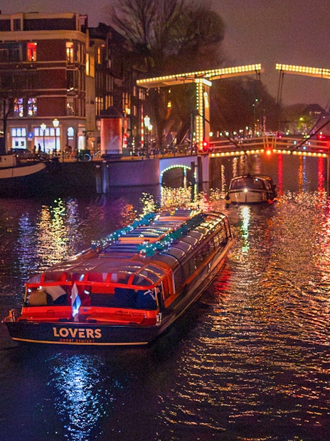 Canal cruise boat under illuminated bridge during Amsterdam Light Festival.