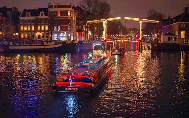 Canal cruise boat under illuminated bridge during Amsterdam Light Festival.