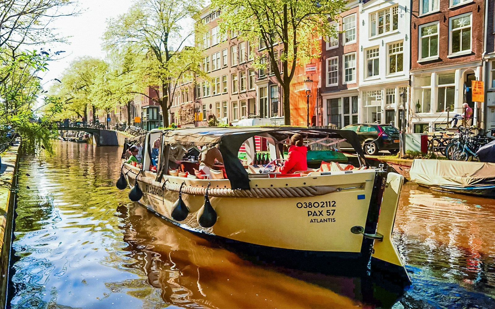 Luxury open boat cruising through Amsterdam canals with passengers enjoying drinks.