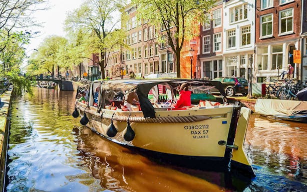 Luxury open boat cruising through Amsterdam canals with passengers enjoying drinks.