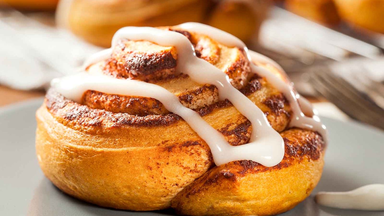 Homemade cinnamon roll pastry with icing on a plate.