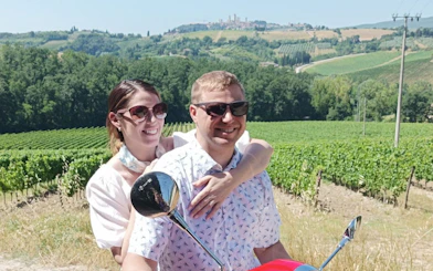 Couple riding a Vespa through Chianti vineyards with San Gimignano in the background.