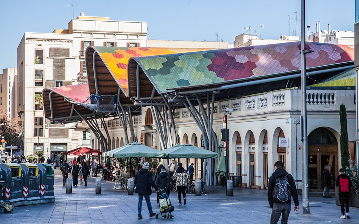 Colorful roof of Mercat de Santa Caterina in Barcelona with people walking nearby.
