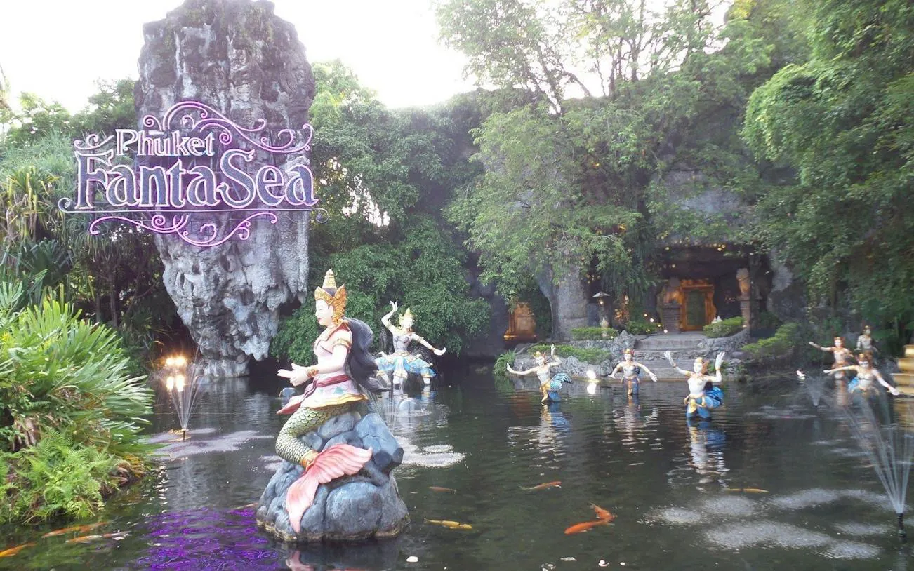 Phuket FantaSea entrance with statues in a pond surrounded by lush greenery.