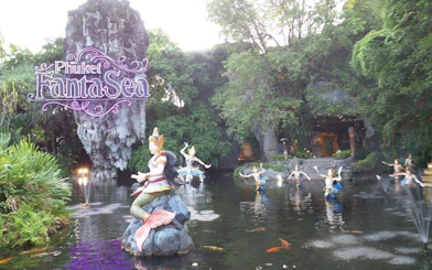 Phuket FantaSea entrance with statues in a pond surrounded by lush greenery.