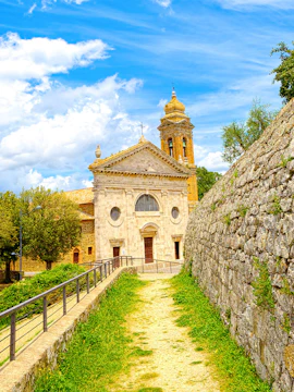 Historic church with bell tower in Montalcino, Italy, surrounded by stone walls and greenery.