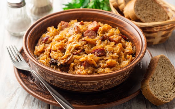 Bowl of traditional Polish Bigos stew with bread on a wooden table.