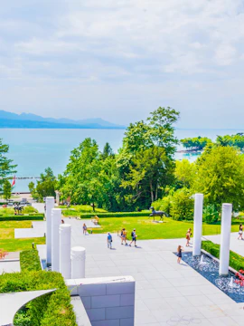 Visitors walking through the gardens of The Olympic Museum in Lausanne, Switzerland, with Lake Geneva in the background.