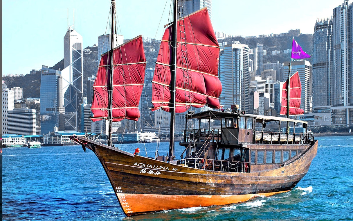 Traditional junk boat with red sails in Hong Kong's Victoria Harbor during AquaLuna day tour.