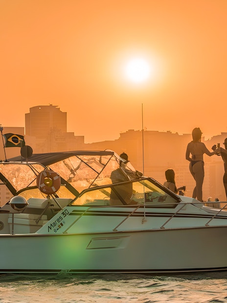 Tourists enjoying a sunset cruise in Rio de Janeiro with city skyline in the background.