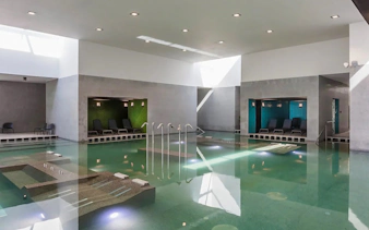 Indoor pool at Pesterzsebet Bath, Budapest with lounge chairs and modern design.