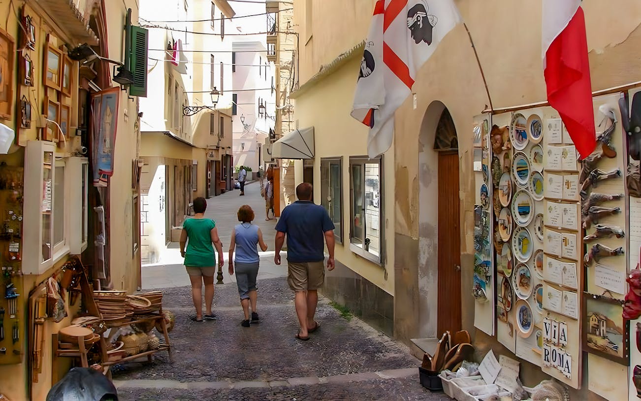 Tourists walking through a narrow street in Alghero's historic center, Sardinia.