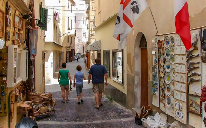 Tourists walking through a narrow street in Alghero's historic center, Sardinia.