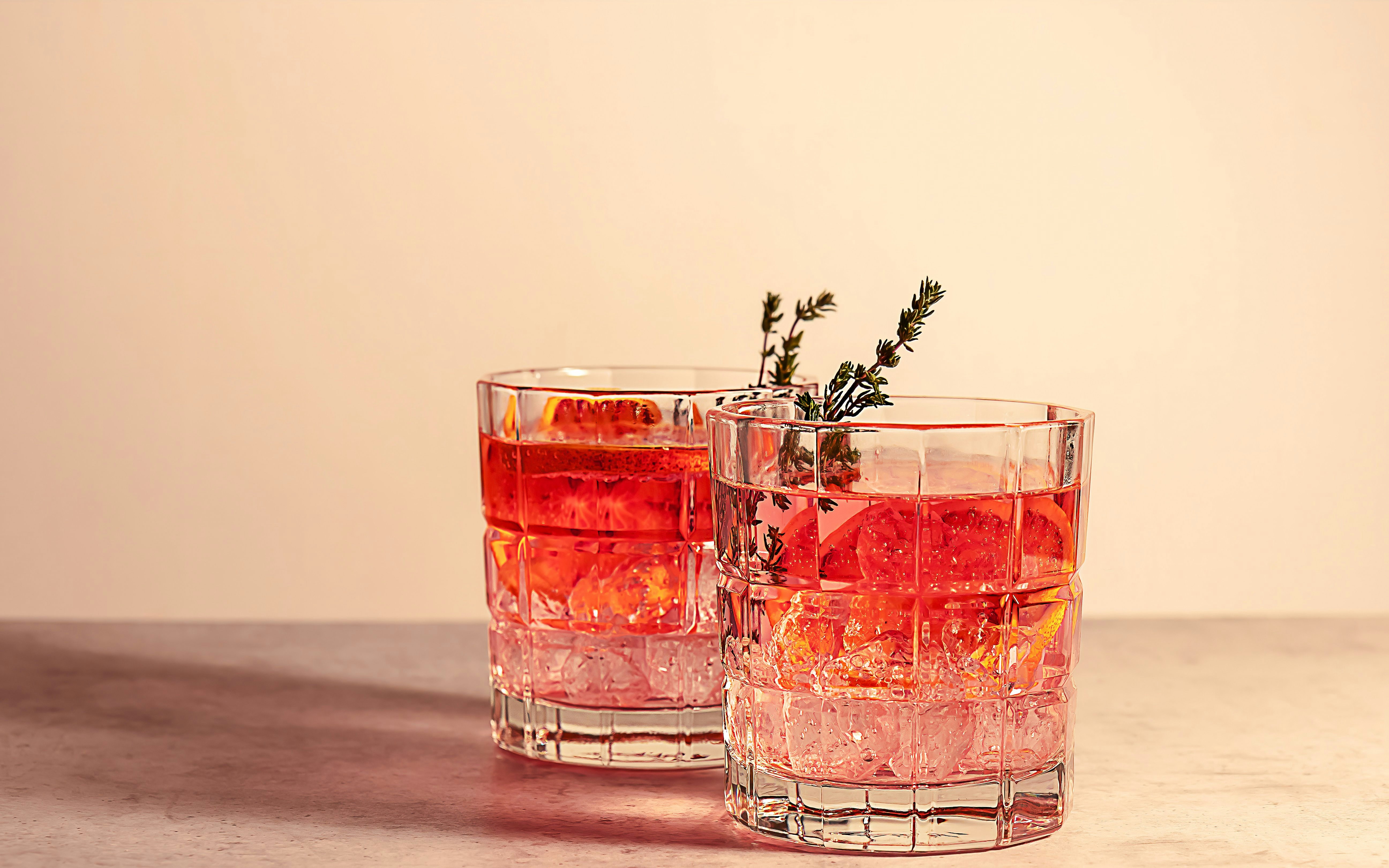 Two glasses of red gin cocktail with ice and garnished with herbs.