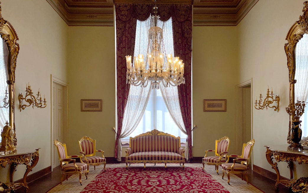 Interior of Dolmabahçe Palace with chandelier, ornate furniture, and red carpet in Istanbul, Turkey.