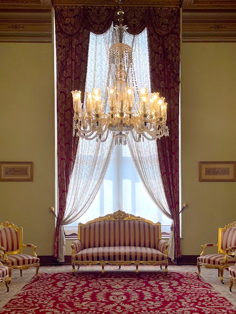 Interior of Dolmabahçe Palace with chandelier, ornate furniture, and red carpet in Istanbul, Turkey.