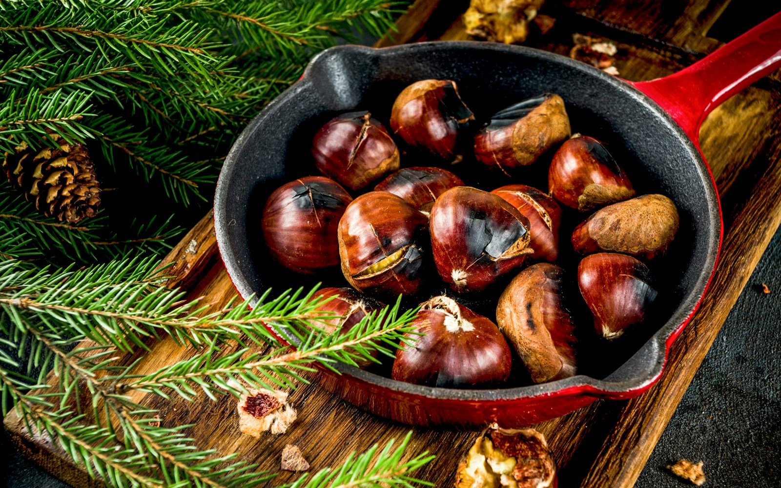 Roasted chestnuts in a red pan with pine branches nearby.