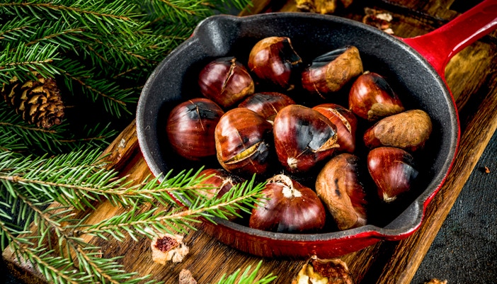 Roasted chestnuts in a red pan with pine branches nearby.