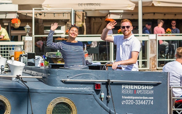 People waving on a canal cruise boat in Amsterdam.