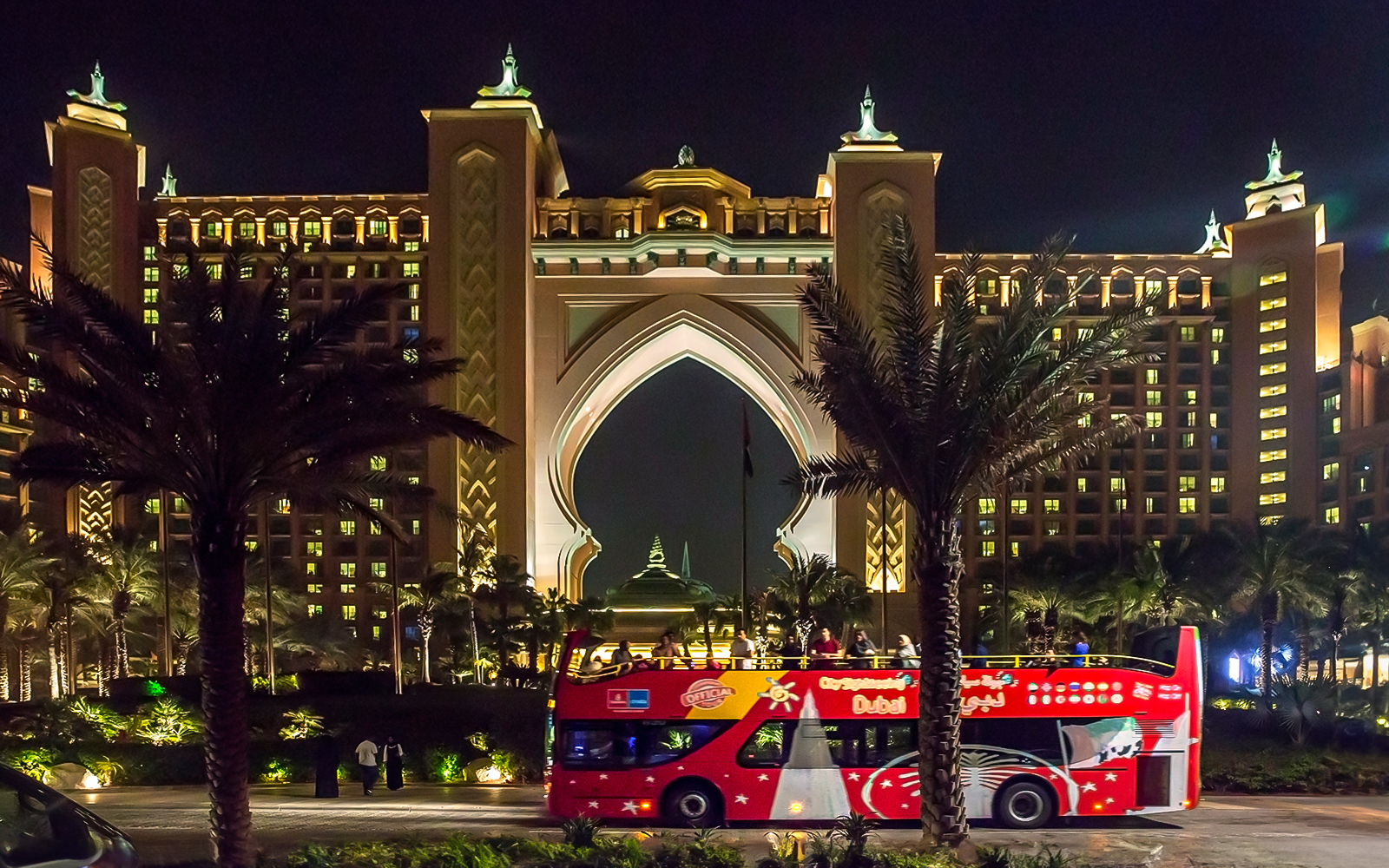 Open-top tour bus in front of Atlantis Hotel, Dubai at night.