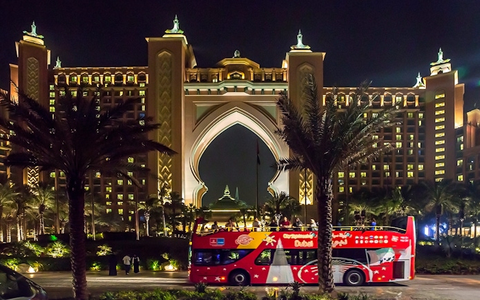 Open-top tour bus in front of Atlantis Hotel, Dubai at night.
