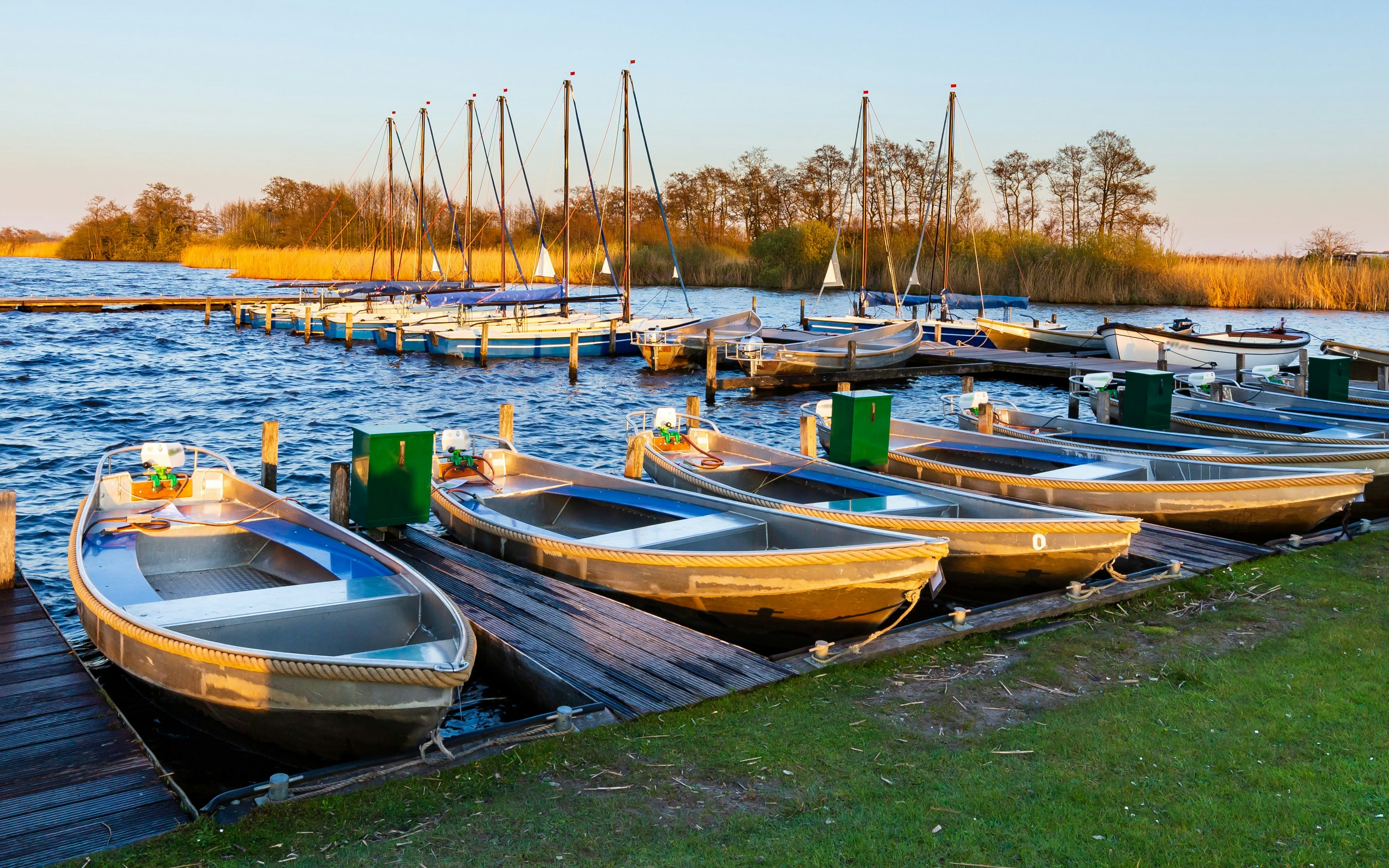 Boats docked at Groningen marina with calm water and surrounding reeds.