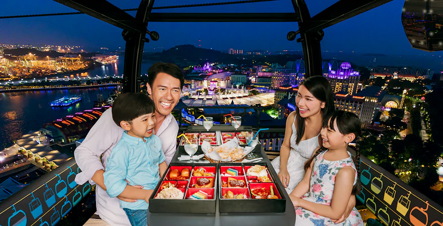 Family dining in Singapore cable car with city lights view.
