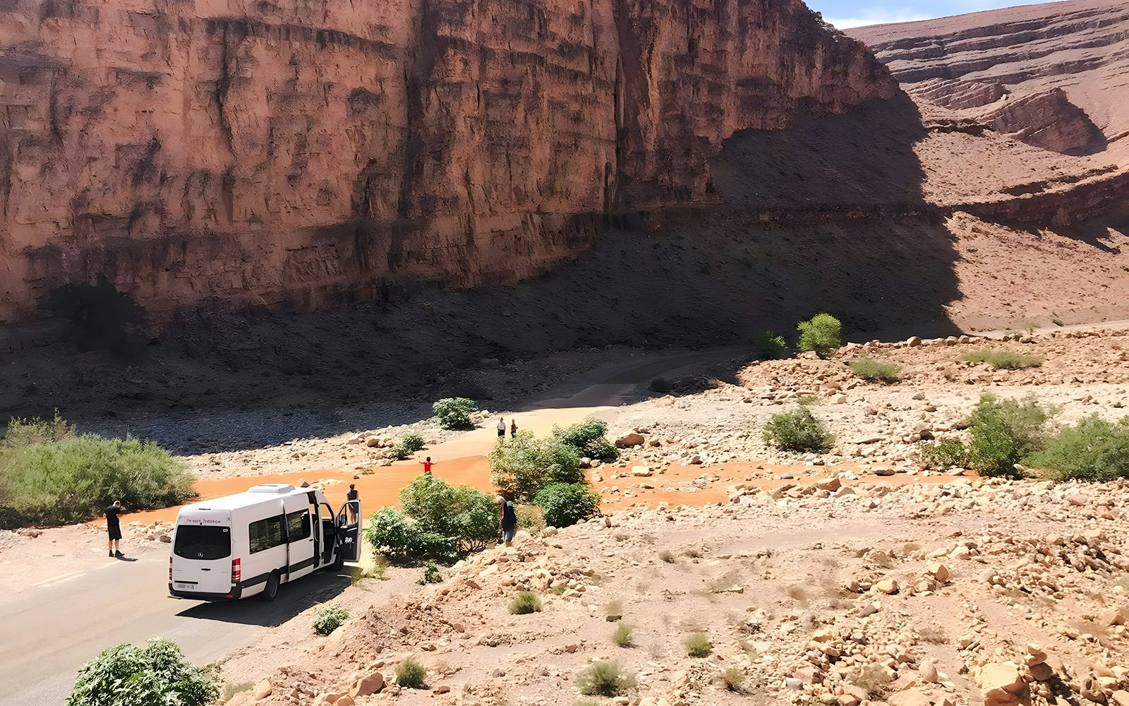 Van traveling through rocky terrain in Agafay Desert, Marrakech, with desert mountains in the background.