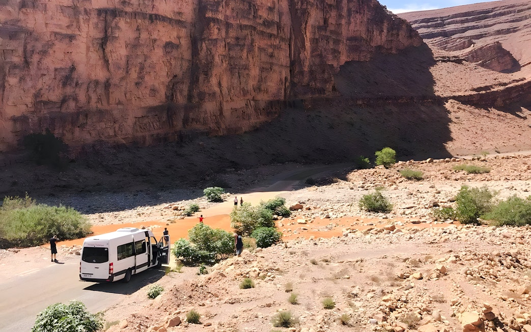 Van traveling through rocky terrain in Agafay Desert, Marrakech, with desert mountains in the background.