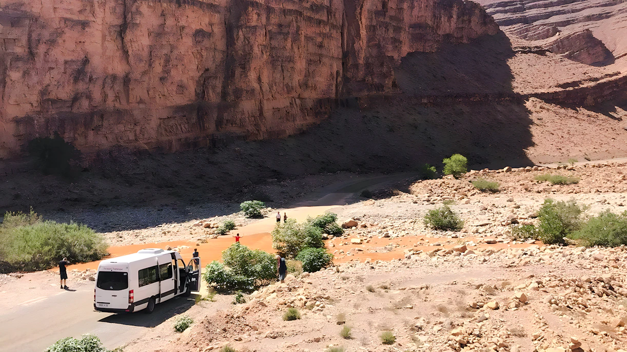 Van traveling through rocky terrain in Agafay Desert, Marrakech, with desert mountains in the background.